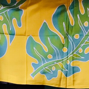 May include: Yellow fabric with a repeating pattern of large tropical leaves. The leaves are green and blue with white outlines, set against a bright yellow background. The design is likely for home decor or apparel.