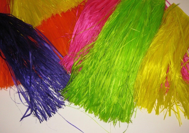 May include: A collection of vibrant, multi-colored raffia-style fringe strips in shades of deep purple, bright lime green, hot pink, orange, and yellow. The material consists of thin, fibrous strands arranged in overlapping layers with a glossy finish.