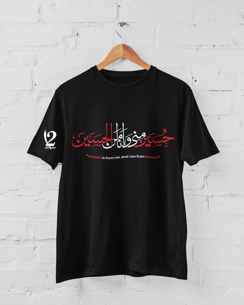 K&ouml;nnte beinhalten: Schwarzes T-Shirt mit roter und wei&szlig;er arabischer Kalligraphie und dem englischen Text "Hussain is from me, and I am from Hussain." Das Shirt hat auch ein Logo auf dem linken &Auml;rmel.