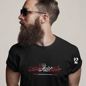 K&ouml;nnte beinhalten: Schwarzes T-Shirt mit roter und wei&szlig;er arabischer Kalligraphie und dem englischen Text "Hussain is from me, and I am from Hussain." Das Shirt hat einen Rundhalsausschnitt und kurze &Auml;rmel. Ein Logo ist auf der rechten Schulter sichtbar.