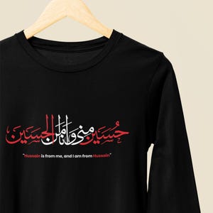K&ouml;nnte beinhalten: Schwarzes Langarmshirt mit roter und wei&szlig;er arabischer Kalligraphie und dem englischen Text "Hussain is from me, and I am from Hussain." Das Shirt hat einen Rundhalsausschnitt und ein Logo auf dem &Auml;rmel.