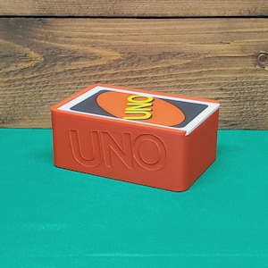 May include: A red rectangular box of UNO playing cards. The word "UNO" is embossed on the front of the box. The top of the box features the UNO logo on a card.