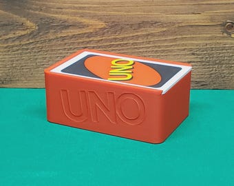 May include: A red rectangular box of UNO playing cards. The word "UNO" is embossed on the front of the box. The top of the box features the UNO logo on a card.