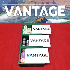 Op de afbeelding: Een groene spelorganizer met drie compartimenten met spelonderdelen. Elke sectie bevat witte kaarten met het woord "VANTAGE" en dobbelstenen of tokens. De afbeelding toont het woord "VANTAGE" in wit.