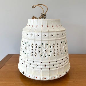 May include: A bell-shaped pendant light fitting with a white textured surface featuring vertical grooves and horizontal bands. The exterior is decorated with small, inlaid circular beads in red, green, and dark blue, arranged in floral and geometric patterns.