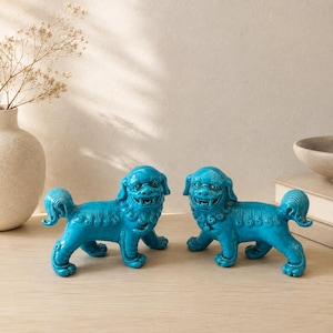 May include: A pair of bright turquoise ceramic Foo dog statues, each featuring intricate sculpted manes, tails, and open-mouthed expressions. These guardian lion figures are depicted in a standing position with detailed fur textures and smooth, glossy finishes.