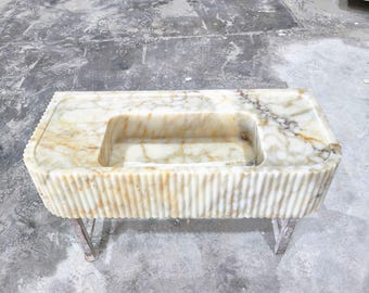 Op de afbeelding: Een witte marmeren badkamer wastafel met een rechthoekig bassin en een geflute basis. De wastafel wordt ondersteund door twee metalen poten.