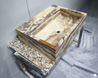 Op de afbeelding: Rechthoekige onyx badkamer wastafel met een natuurlijk, gelaagd patroon van beige, bruine en crèmekleuren. De wastafel heeft twee kraangaten en een afvoergat. Hij staat op een metalen standaard en een decoratief aanrecht.