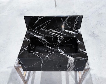 May include: A rectangular black marble sink with white veining. The sink has a built-in backsplash and is supported by a metal frame. The polished surface reflects light, highlighting the natural stone pattern.