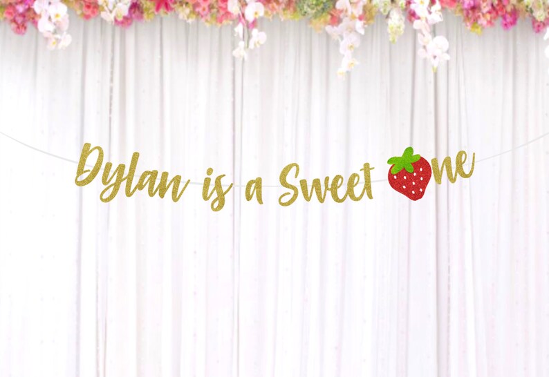 Op de afbeelding: Gouden glitterbanner met de tekst "Dylan is a Sweet One" en een rode aardbeienafbeelding.