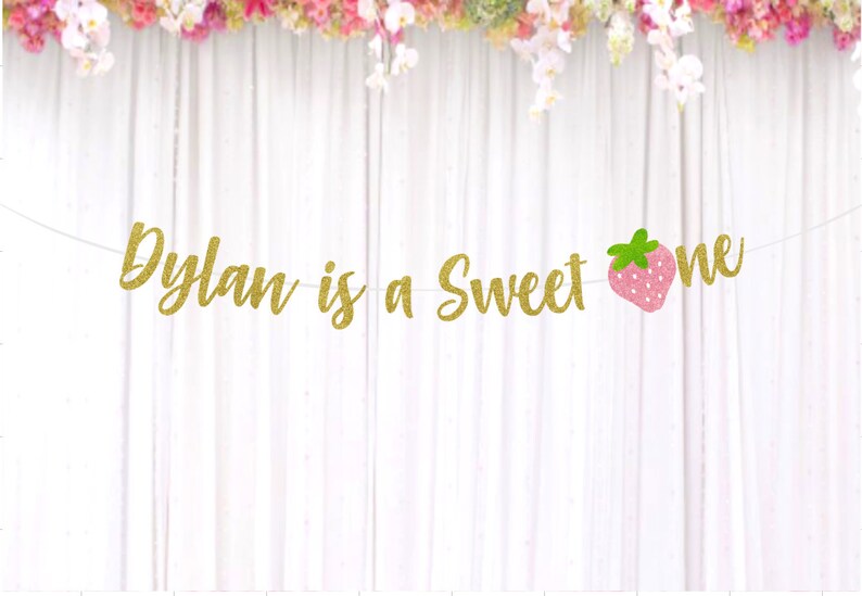 Op de afbeelding: Gouden glitterbanner met de tekst "Dylan is a sweet one" en een roze aardbeienafbeelding.