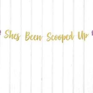 Puede incluir: Pancarta de purpurina dorada con el texto "She's Been Scooped Up" y dos recortes de conos de helado morados.