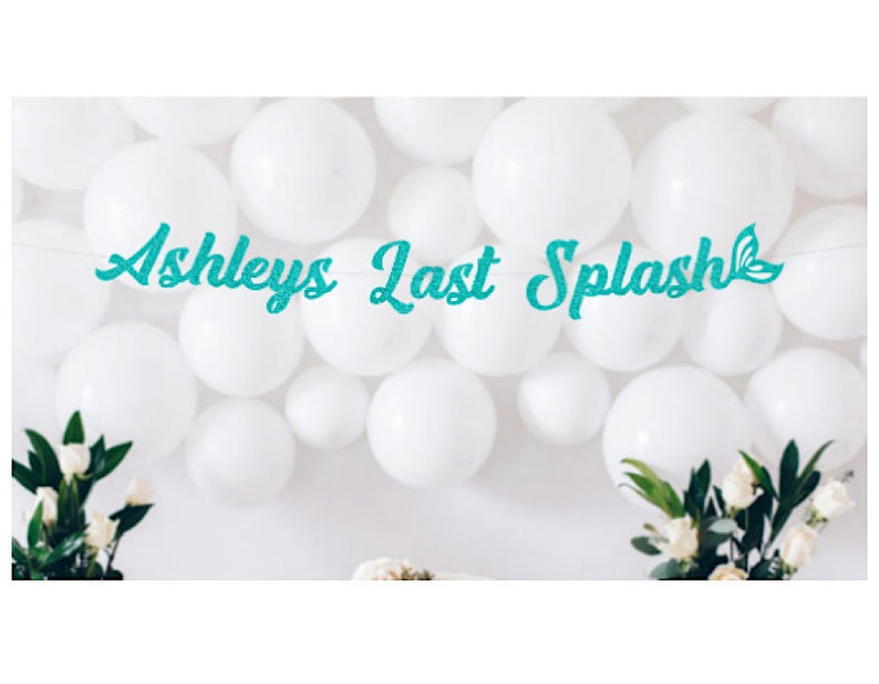 May include: A teal glitter banner with the text "Ashleys Last Splash" and a mermaid tail symbol. The banner is hanging in front of a white wall decorated with white balloons.