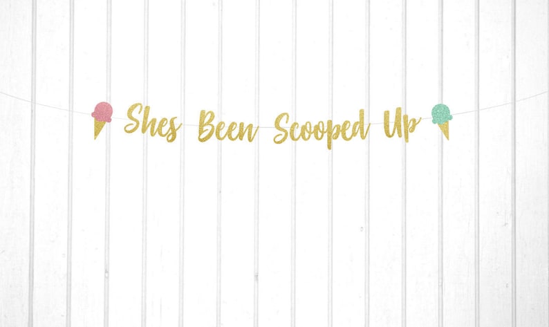 May include: Gold glitter banner with the text "She's Been Scooped Up" and two ice cream cone cutouts, one pink and one blue.