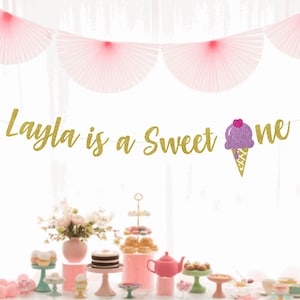 May include: Gold glitter banner with the text "Layla is a Sweet One" and a purple and pink ice cream cone graphic.
