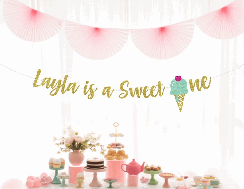 May include: Gold glitter banner with the text "Layla is a Sweet One" and a green and pink glitter ice cream cone.