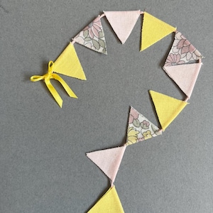 May include: A yellow and pink fabric bunting with a floral pattern. The bunting is strung together with a yellow ribbon.