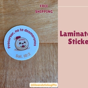 May include: A round, laminated sticker with a light blue background and a cartoon marzipan character. The sticker has text in Spanish, including "Precursor, no te desmorones" and "Sal. 18:2". The words "Laminated Stickers" are also visible.
