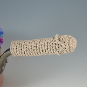 May include: A beige crocheted pot handle cover with a rounded end. The handle cover is on a copper pot.