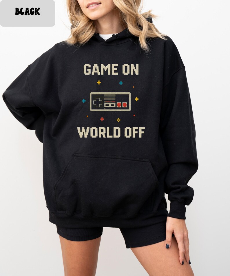 May include: Black hoodie with a pixelated video game controller graphic. The text "GAME ON WORLD OFF" is printed above and below the controller. The hoodie has a front pocket and a hood.