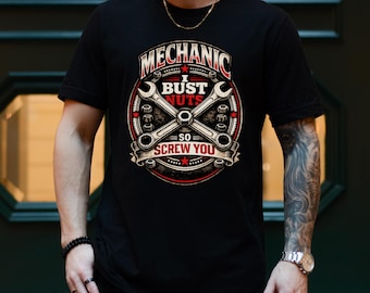 May include: A black short-sleeved t-shirt featuring a graphic design with two crossed wrenches, nuts, and the text "MECHANIC I BUST NUTS SO SCREW YOU" in white and red lettering. The design is circular with red stars and a distressed texture.