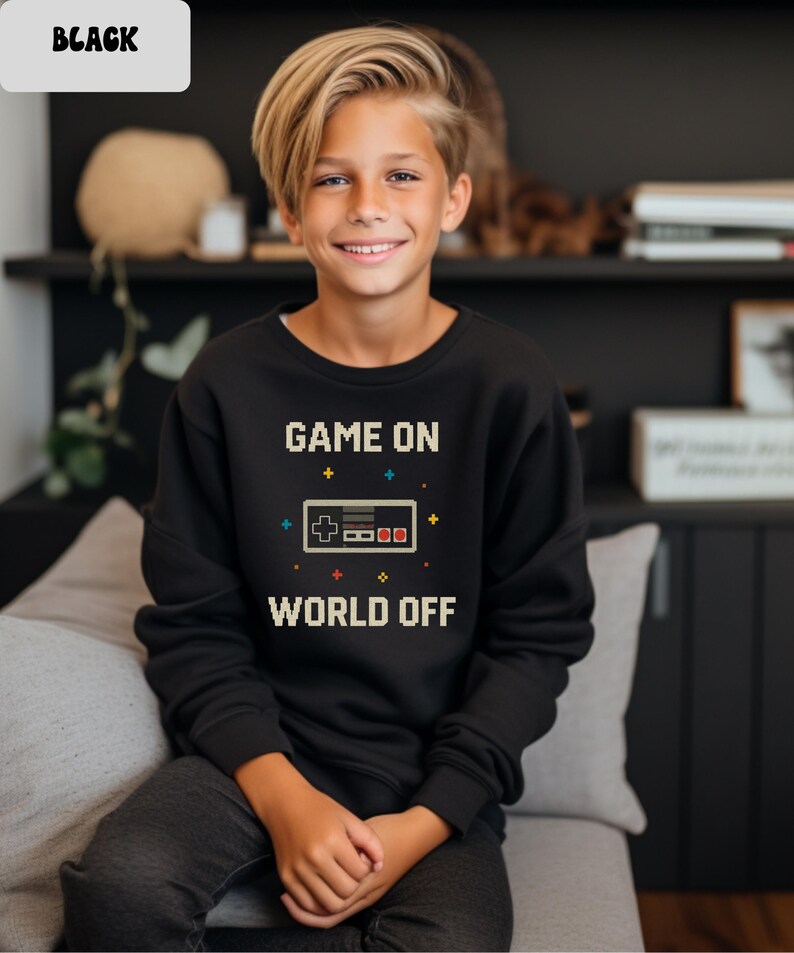 May include: Black sweatshirt with the text "GAME ON WORLD OFF" and a pixelated video game controller graphic. The sweatshirt is worn by a person.