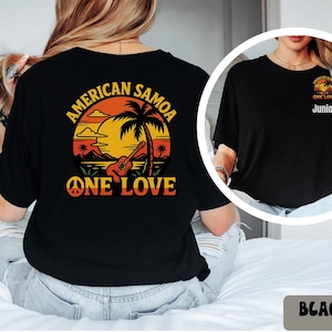 May include: Black t-shirt featuring a vibrant graphic of a sunset scene with palm trees, a guitar, and the text "AMERICAN SAMOA ONE LOVE." A smaller version of the design is on the front, with the word "Junior" below it.
