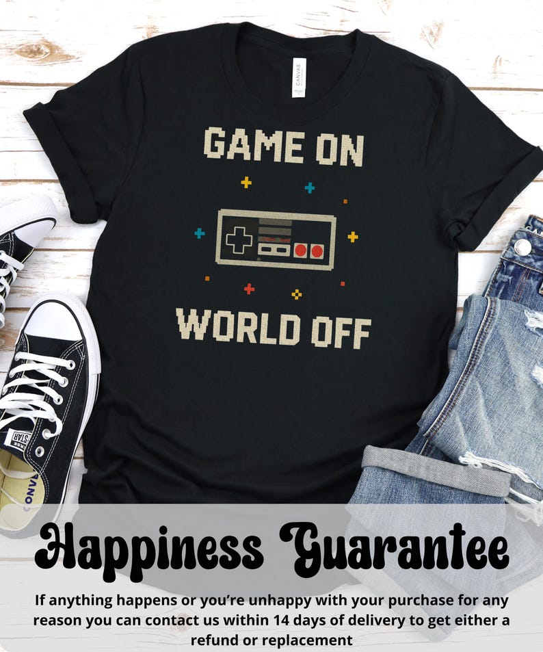 May include: Black t-shirt with the text "GAME ON WORLD OFF" in pixelated font, featuring a pixelated video game controller. The shirt is paired with black and white sneakers and blue jeans. The shirt also has a "Happiness Guarantee" message.