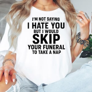 May include: White t-shirt with the text "I'M NOT SAYING I HATE YOU BUT I WOULD SKIP YOUR FUNERAL TO TAKE A NAP" in black. The word "WHITE" is at the bottom of the shirt. The shirt is being worn.