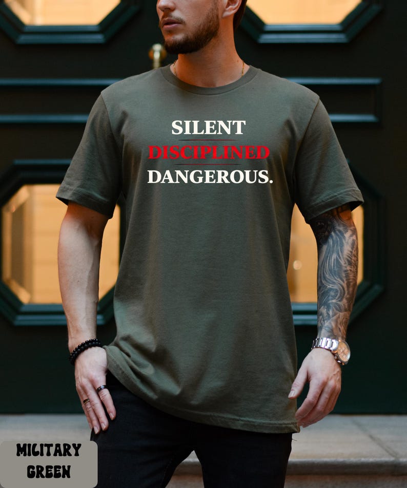 May include: Military green t-shirt with the words "SILENT DISCIPLINED DANGEROUS" in white and red lettering. The shirt is a solid color and has short sleeves. The shirt is made of a soft, comfortable material.