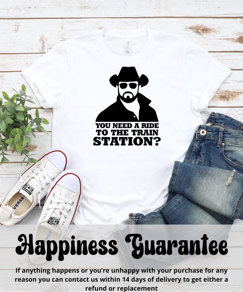K&ouml;nnte beinhalten: Wei&szlig;es T-Shirt mit einer schwarzen Grafik eines Mannes mit Cowboyhut und Sonnenbrille, mit dem Text "YOU NEED A RIDE TO THE TRAIN STATION?". Das Shirt wird mit blauen Jeans und wei&szlig;en Turnschuhen gezeigt.