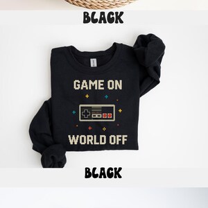 May include: Black t-shirts with the text "GAME ON WORLD OFF" and a pixelated controller graphic. The image shows a t-shirt, a long-sleeve shirt, and a hoodie. The word "BLACK" is displayed below each shirt.