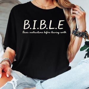May include: Black t-shirt with the acronym "B.I.B.L.E." in white, with the words "Basic instructions before leaving earth" underneath. The shirt is short-sleeved and has a crew neck.