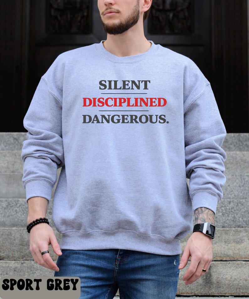 May include: A light gray sweatshirt with the words "SILENT DISCIPLINED DANGEROUS." printed in black and red. The sweatshirt is a sport grey color.