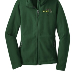 Peut inclure: Une veste polaire vert foncé avec une fermeture éclair complète et un col montant. La veste a deux poches latérales et une petite broderie sur la poitrine avec un cœur, un stéthoscope et le mot "NAME".