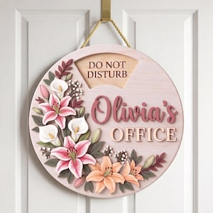 May include: A round wooden door sign with a light pink finish, featuring the text "DO NOT DISTURB" and "Olivia's OFFICE" in raised lettering. The sign is decorated with layered, three-dimensional floral cutouts of pink and white lilies.