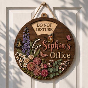 May include: A circular wooden door sign featuring the text DO NOT DISTURB, Sophia's Office, and a floral arrangement with purple, pink, and white flowers, green leaves, and several butterflies in shades of orange, pink, and brown, suspended by a rope.