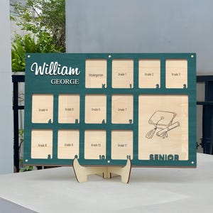 Könnte beinhalten: Eine hölzerne Abschluss-Fototafel in Teal mit Fächern für Fotos vom Kindergarten bis zum Abschlussjahr. Der Name "William GEORGE" steht oben. Das Wort "SENIOR" steht unten, mit einer Illustration von Abschlusskappe und Diplom.
