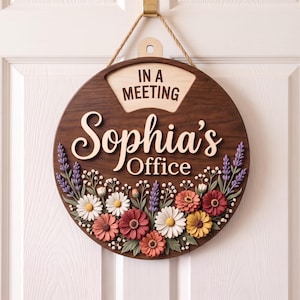 Puede incluir: Un letrero de puerta circular de madera con acabado marrón oscuro que presenta el texto "IN A MEETING" y "Sophia's Office" en relieve. La mitad inferior está decorada con un colorido arreglo de flores y lavanda en tres dimensiones.