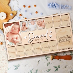 Può includere: Una cornice per foto in legno con 12 spazi per foto, ogni spazio etichettato con un mese. La cornice è personalizzata con il nome "David Darwin" e il testo "Buon compleanno".