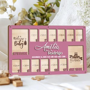 Può includere: Una lavagna di pietra miliare per bambini in legno rosa con spazi per foto e mesi. La lavagna include il nome "Amelia Rodrigo", la data di nascita e il peso. Il testo include "Benvenuto Bebè", "Buon Compleanno" e numeri di mesi.