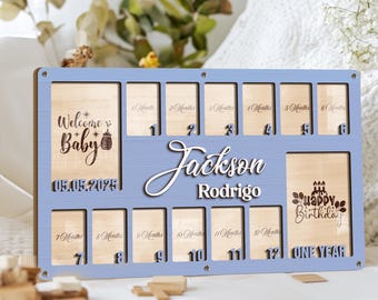 May include: A rectangular light blue wooden baby milestone photo frame featuring the name Jackson Rodrigo in white script. It includes twelve small slots labeled 1 to 12 months, a Welcome Baby section with the date 05.05.2025, and a Happy Birthday section.