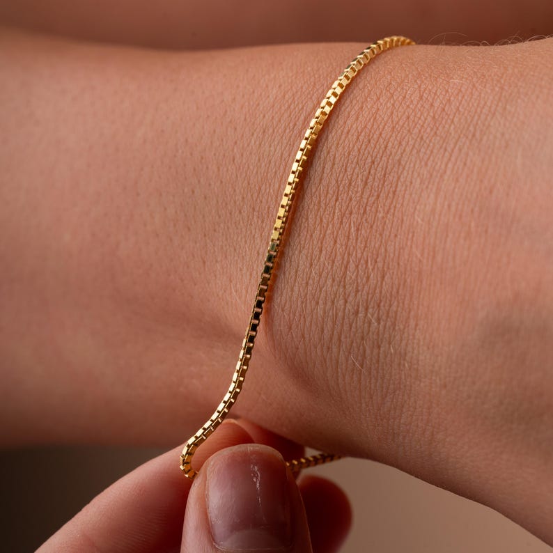 Op de afbeelding: Een gouden kettingarmband met een box chain-ontwerp. De armband zit om een pols.