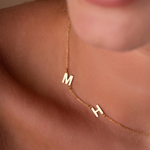 May include: A gold chain necklace with two letter charms, an "M" and an "H", hanging from it.