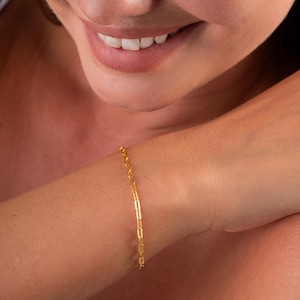 Op de afbeelding: Een gouden kettingarmband met een delicaat, doosvormig kettingschakelontwerp.