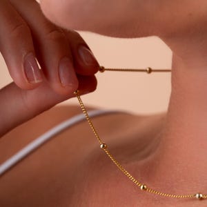 May include: A gold chain necklace with small round beads. The necklace is delicate and simple.