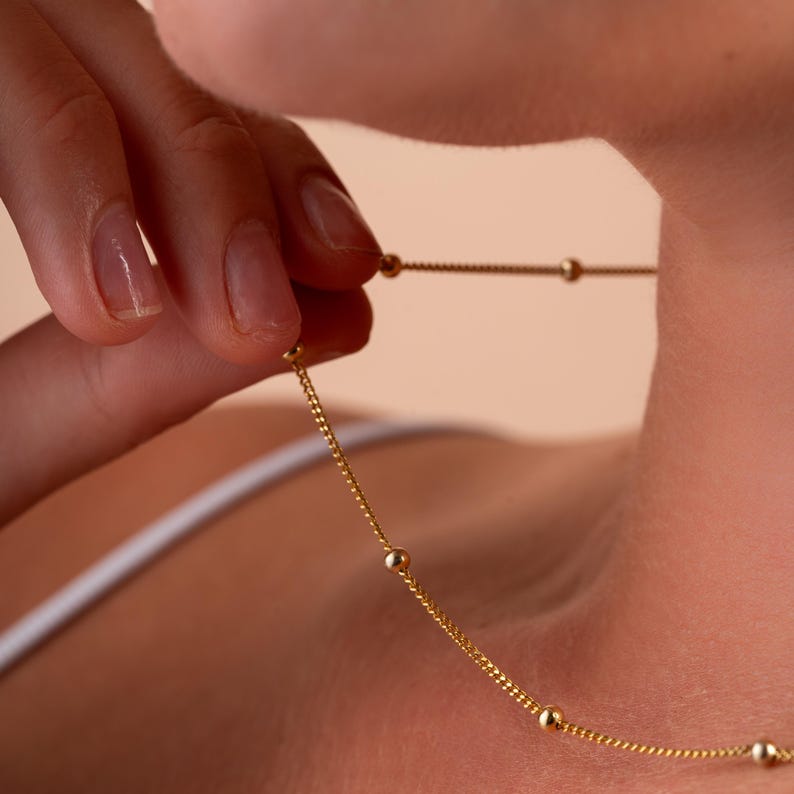 May include: A gold chain necklace with small round beads. The necklace is delicate and simple.