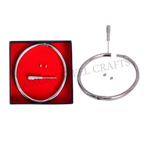 Puede incluir: Un collar de gargantilla de acero plateado con un destornillador y tornillos pequeños. El collar está en una caja roja con la palabra "LUXURY" visible. Las palabras "STEEL CRAFTS" están impresas en el collar.