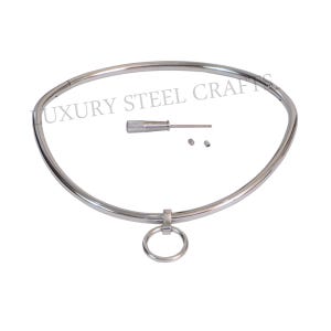 Könnte beinhalten: Eine silberne Metall-Choker-Halskette mit einem runden Ring. Die Halskette ist aus dickem, robustem Metall gefertigt und hat eine glatte Oberfläche. Sie wird mit einem kleinen Schraubendreher und zwei Schrauben zum Einstellen der Größe geliefert.