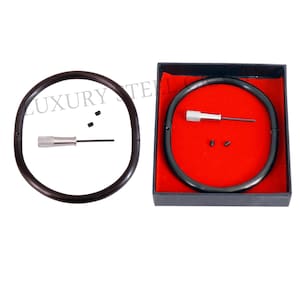 May include: A black circular object with a silver screwdriver and small black pieces. The object is displayed in a black box with a red interior. The text "LUXURY TELL" is visible in the image.